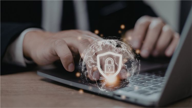 Close-up of hands typing on a laptop with a glowing, digital security shield icon floating above the keyboard.