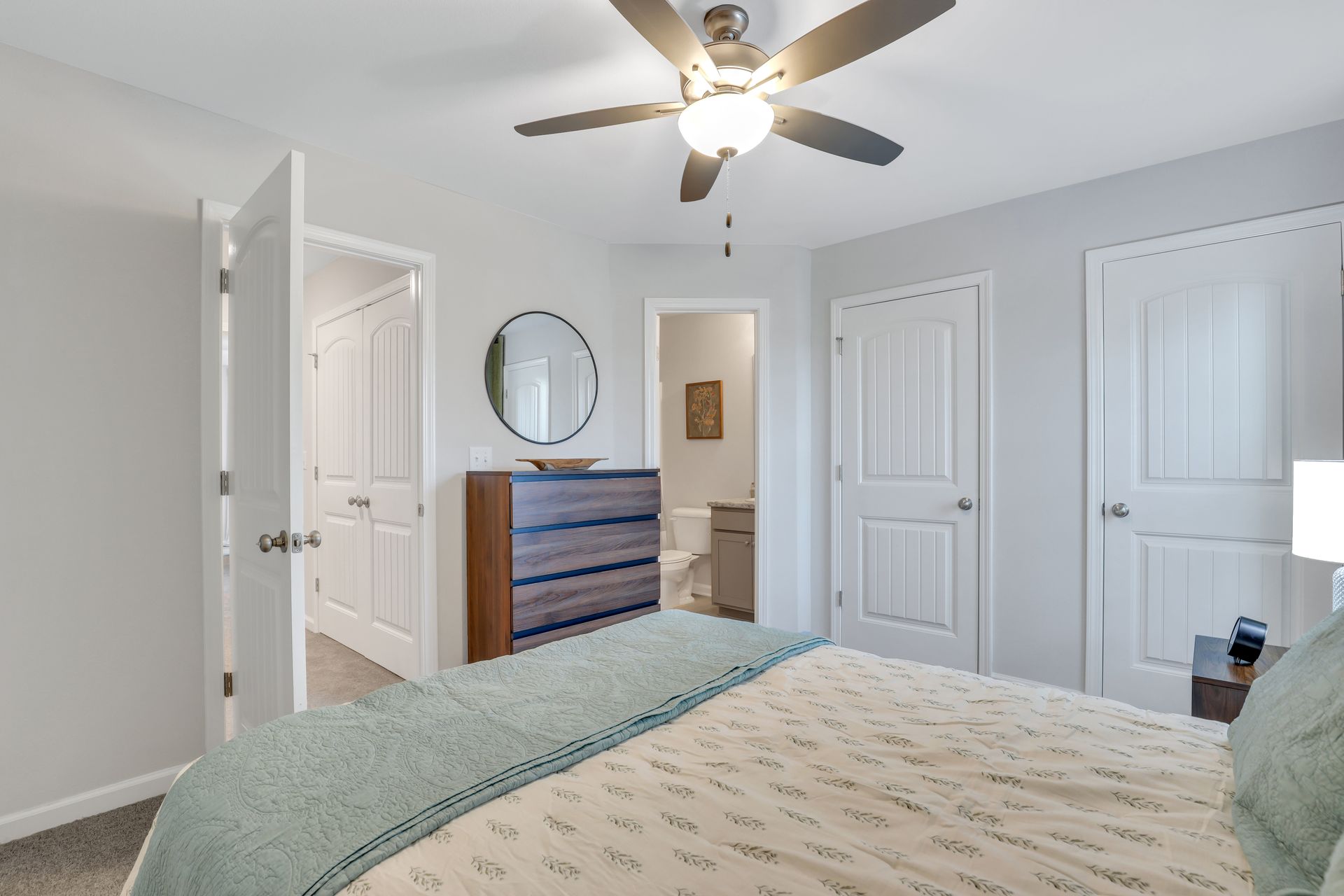 A bedroom with a bed , dresser , mirror and ceiling fan.