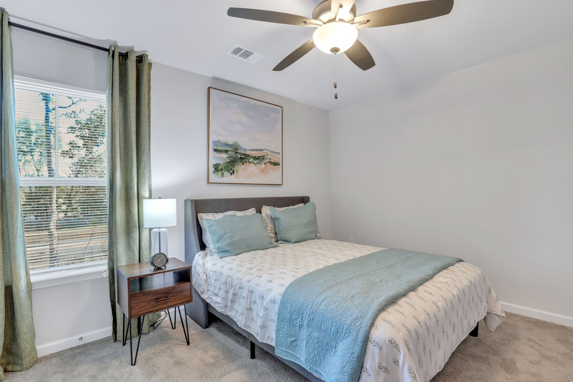 A bedroom with a bed , nightstand , lamp and ceiling fan.