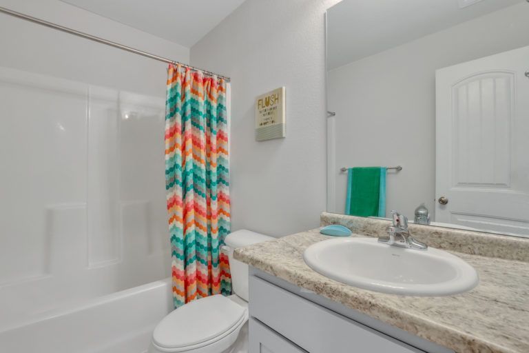 A bathroom with a toilet , sink , shower and mirror.