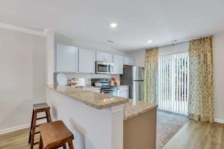 A kitchen with white cabinets , granite counter tops , stainless steel appliances and a sliding glass door.