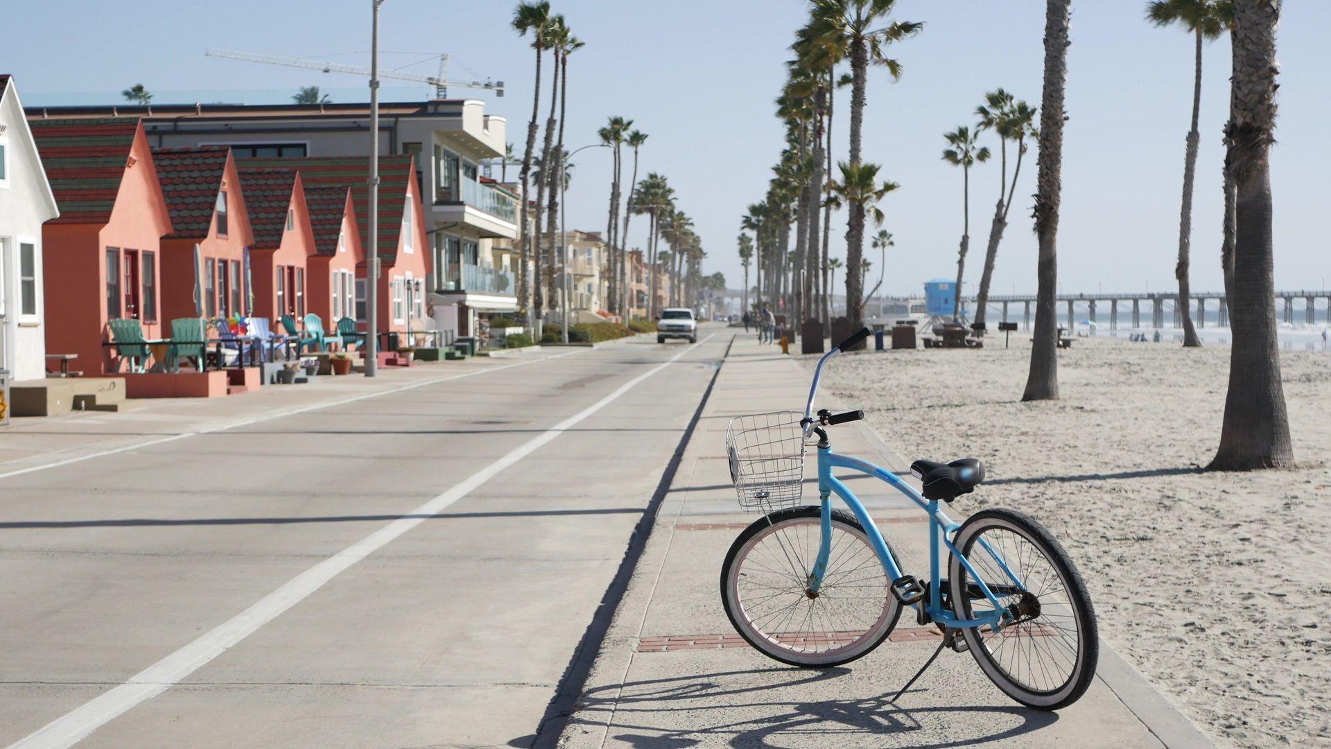 Beach road with a blue bicycle, palm trees, and colorful houses under a bright sky.