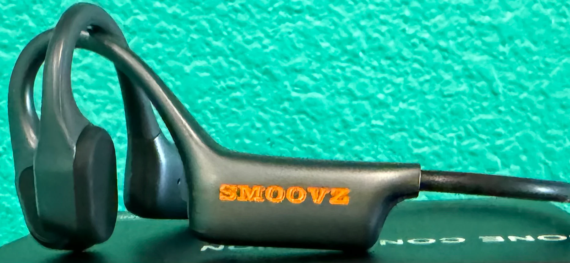 A pair of SMOOVZ open-ear headphones sitting on top of a box on a table.