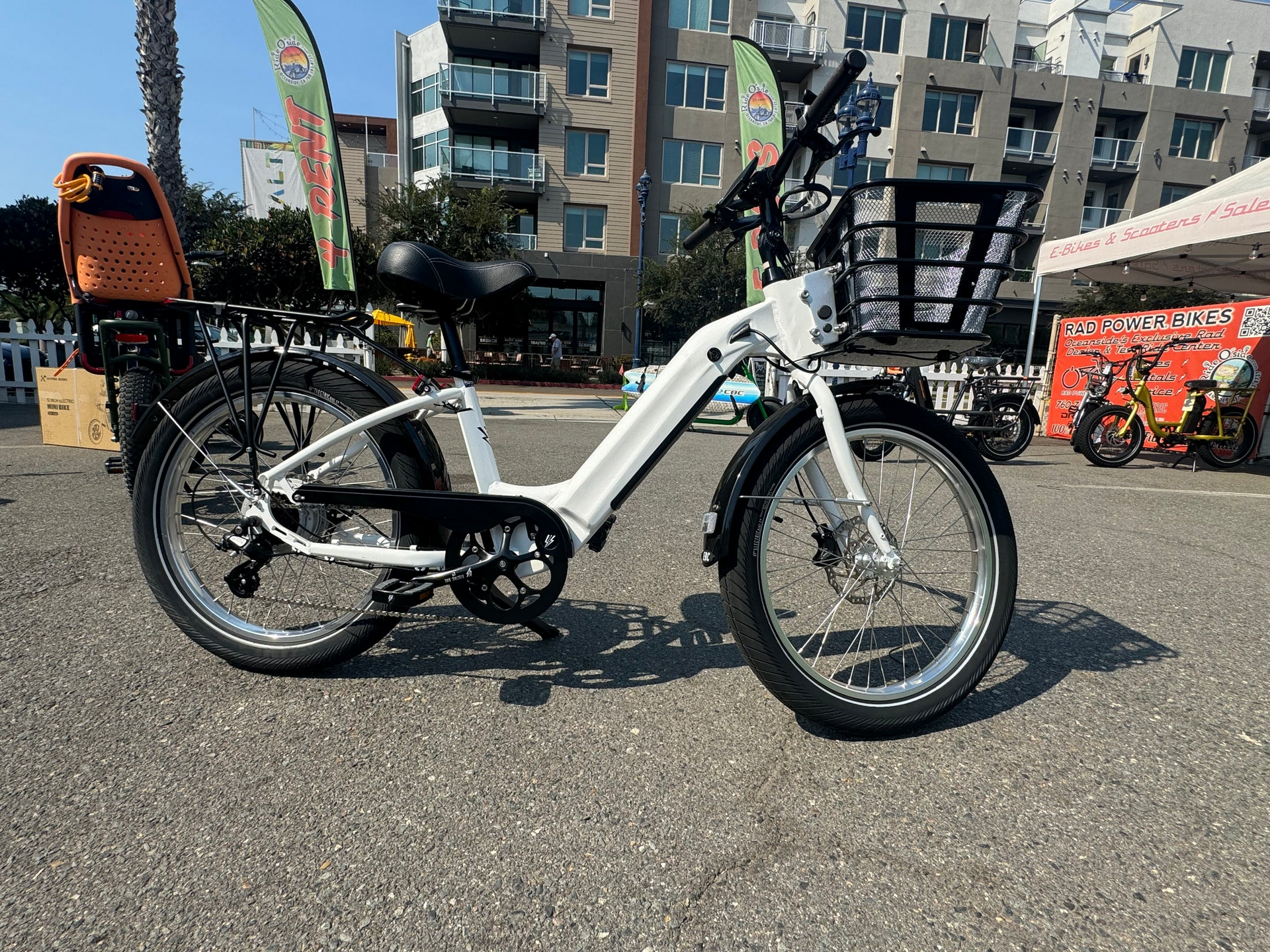 A white electric bike with a basket is parked on the side of the road.