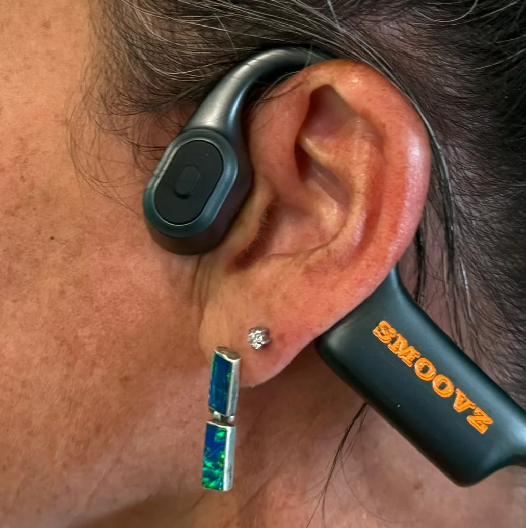 A pair of SMOOVZ open-ear headphones sitting on top of a box on a table.