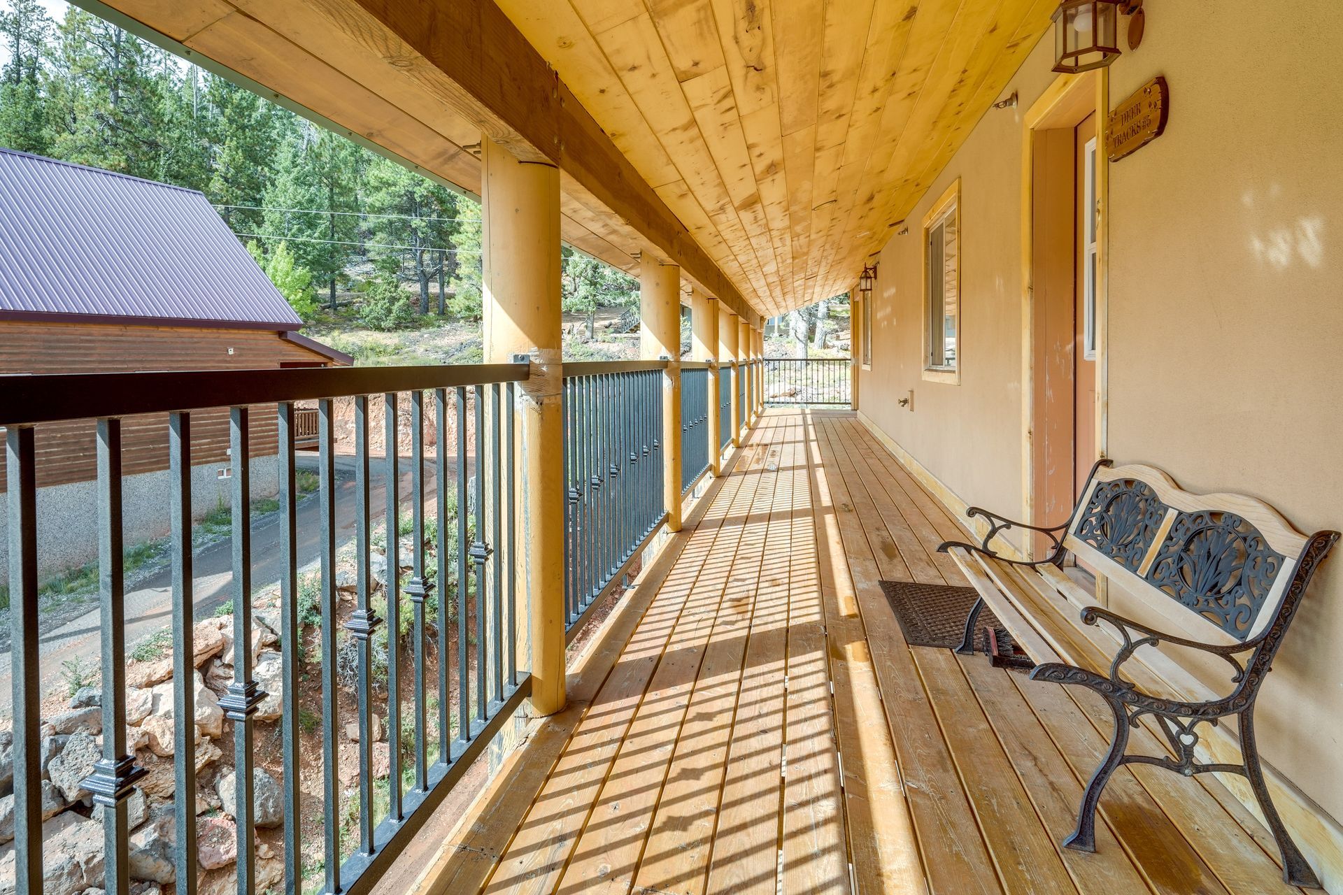 A long, wooden porch with a metal bench. The porch has a railing, support columns, and overlooks a hillside.