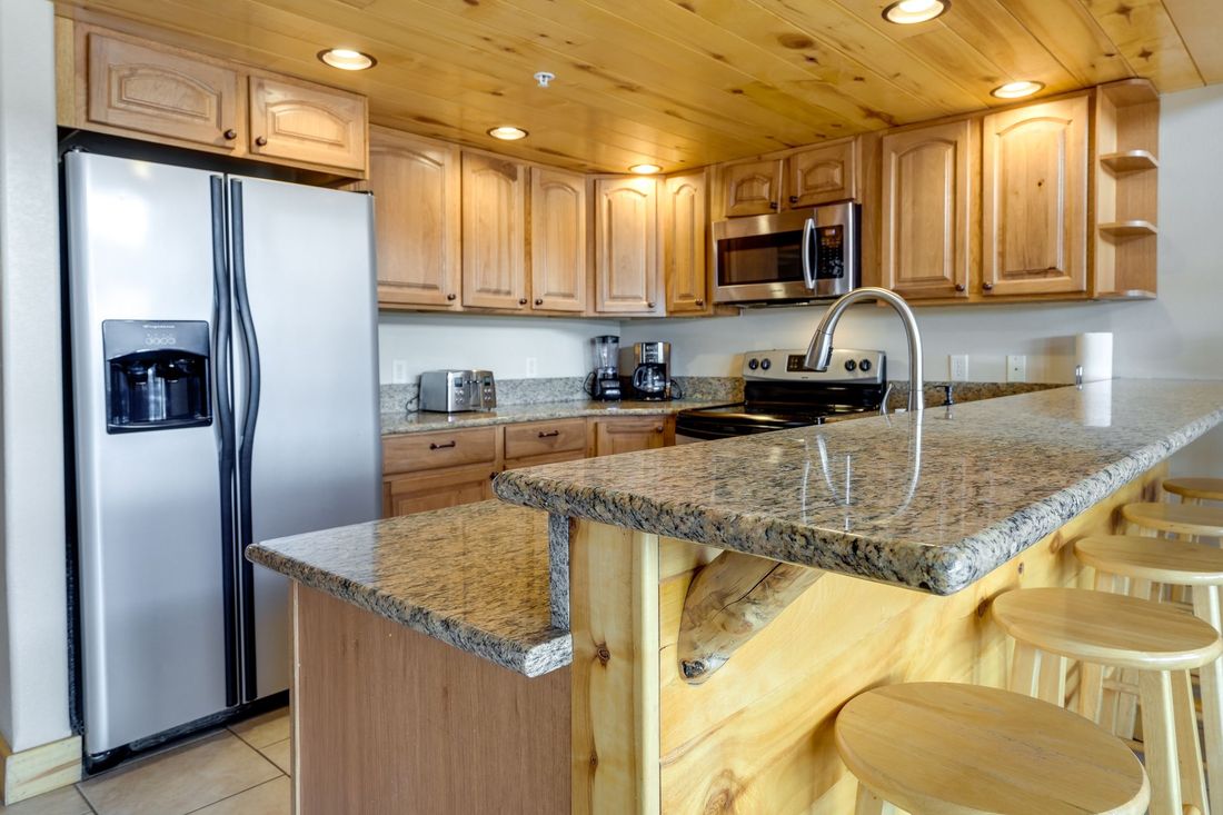 Kitchen with wooden cabinets, granite countertops, stainless steel appliances, and a breakfast bar with stools.