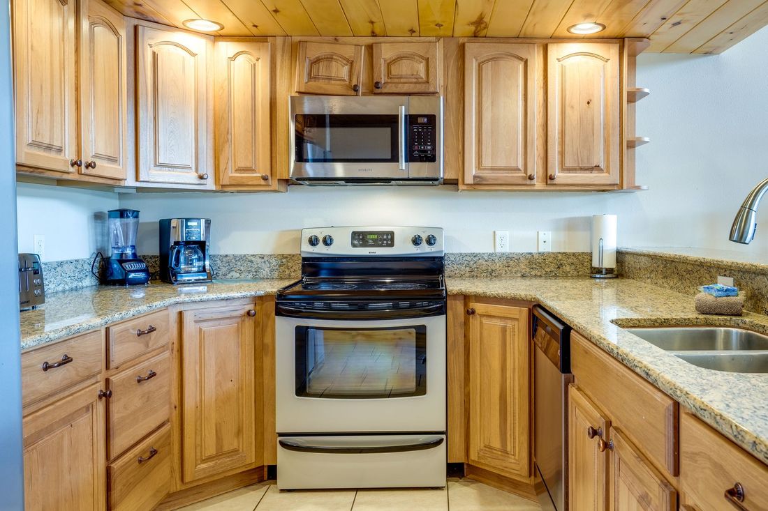 Kitchen with light wood cabinets, granite countertops, and stainless steel appliances, including a microwave and oven.