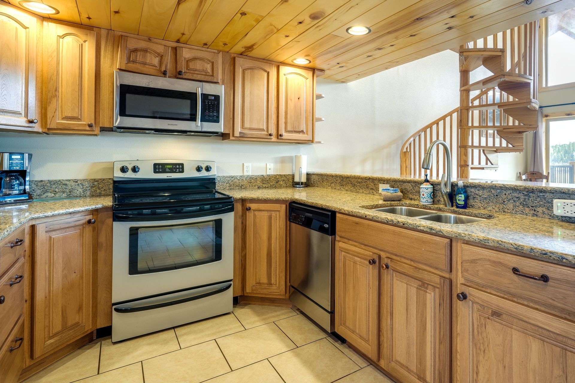 Kitchen with wooden cabinets, stainless steel appliances, granite countertops, and a spiral staircase.
