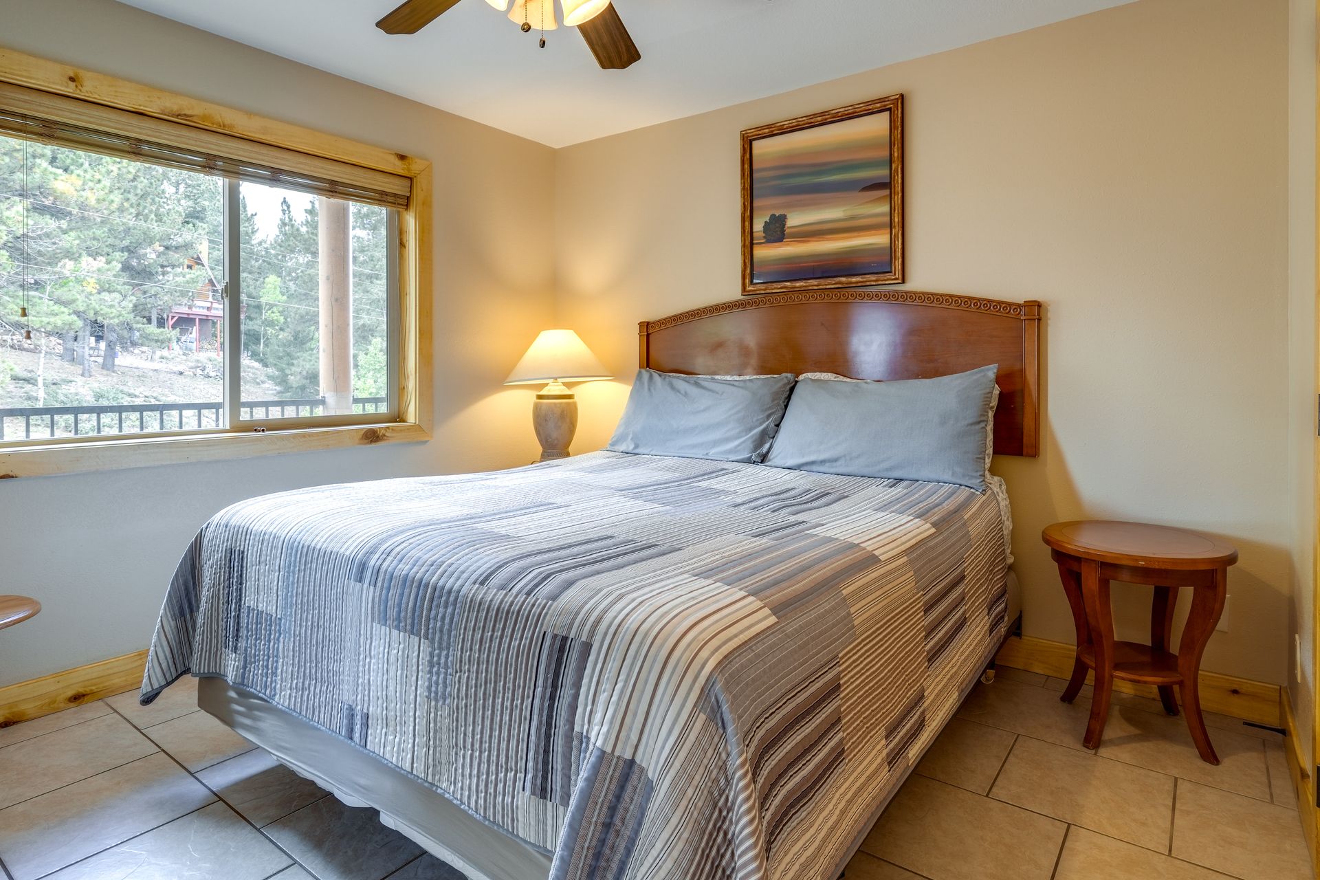 A cozy bedroom with a queen-sized bed, a window overlooking trees, and a bedside table.