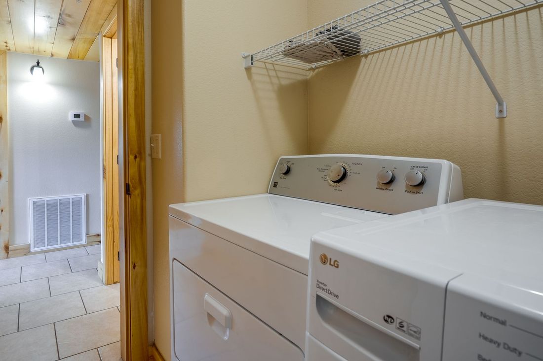 Laundry room with white washer and dryer. A hallway with a light and air vent is visible through the doorway.