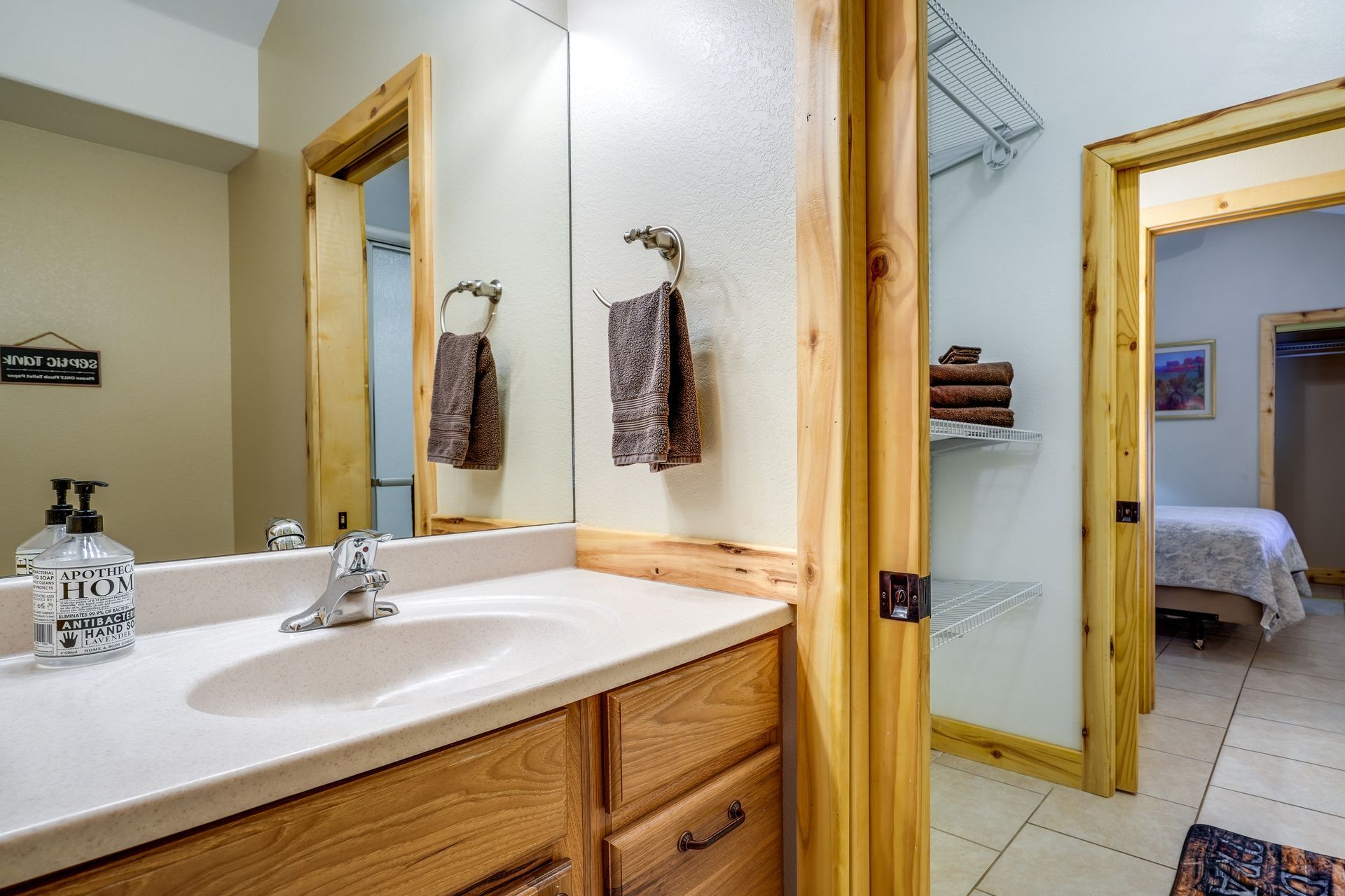 Bathroom with a wooden vanity, mirror, and two doors leading to other rooms. Tan walls and a towel rack are visible.