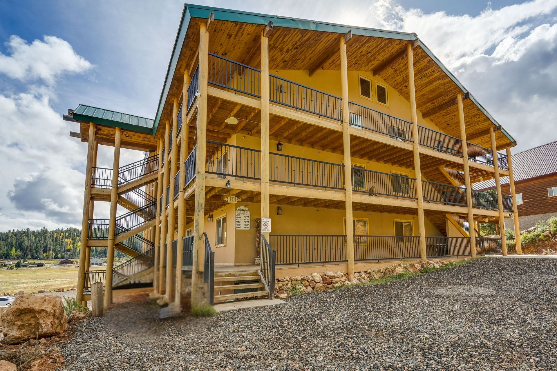 Three-story wooden cabin with balconies, exterior stairs, and an ATV parked in front. Sunny day with a blue sky.
