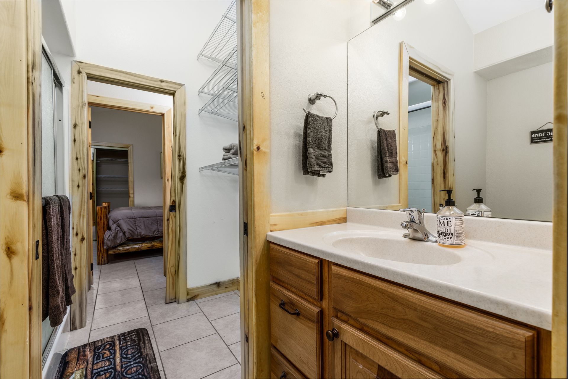 Bathroom with wooden cabinetry and trim, a white sink, and a doorway leading to a bedroom. A towel rack hangs on the mirror.