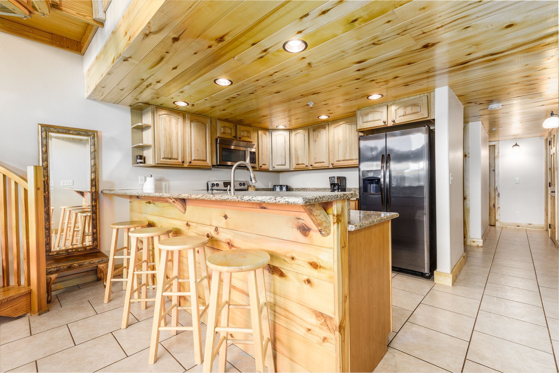 Kitchen with light wood cabinets, granite countertops, and a breakfast bar with three stools.