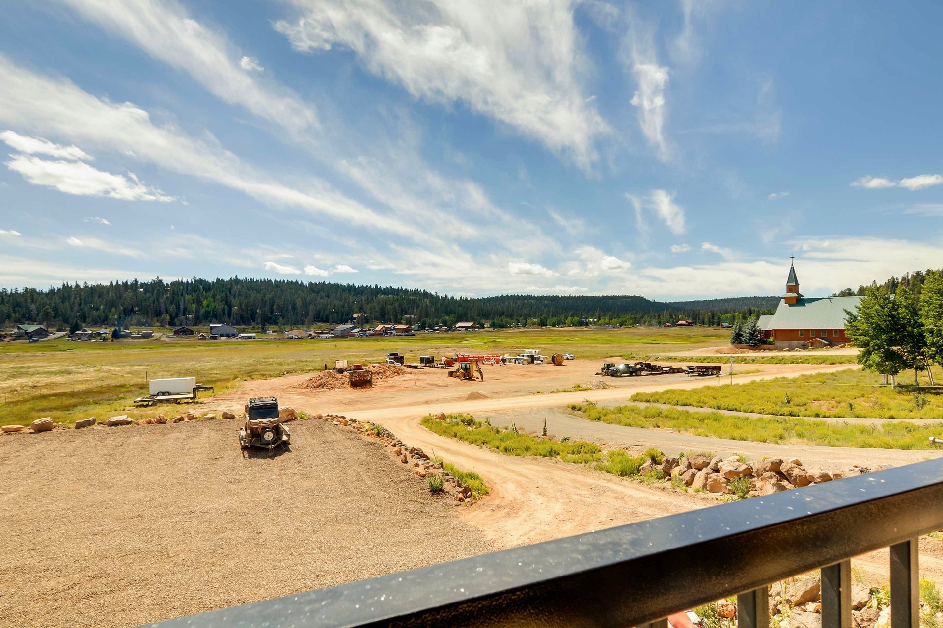 Scenic view of a field with a dirt road and construction equipment, a building with a steeple, and a distant treeline.