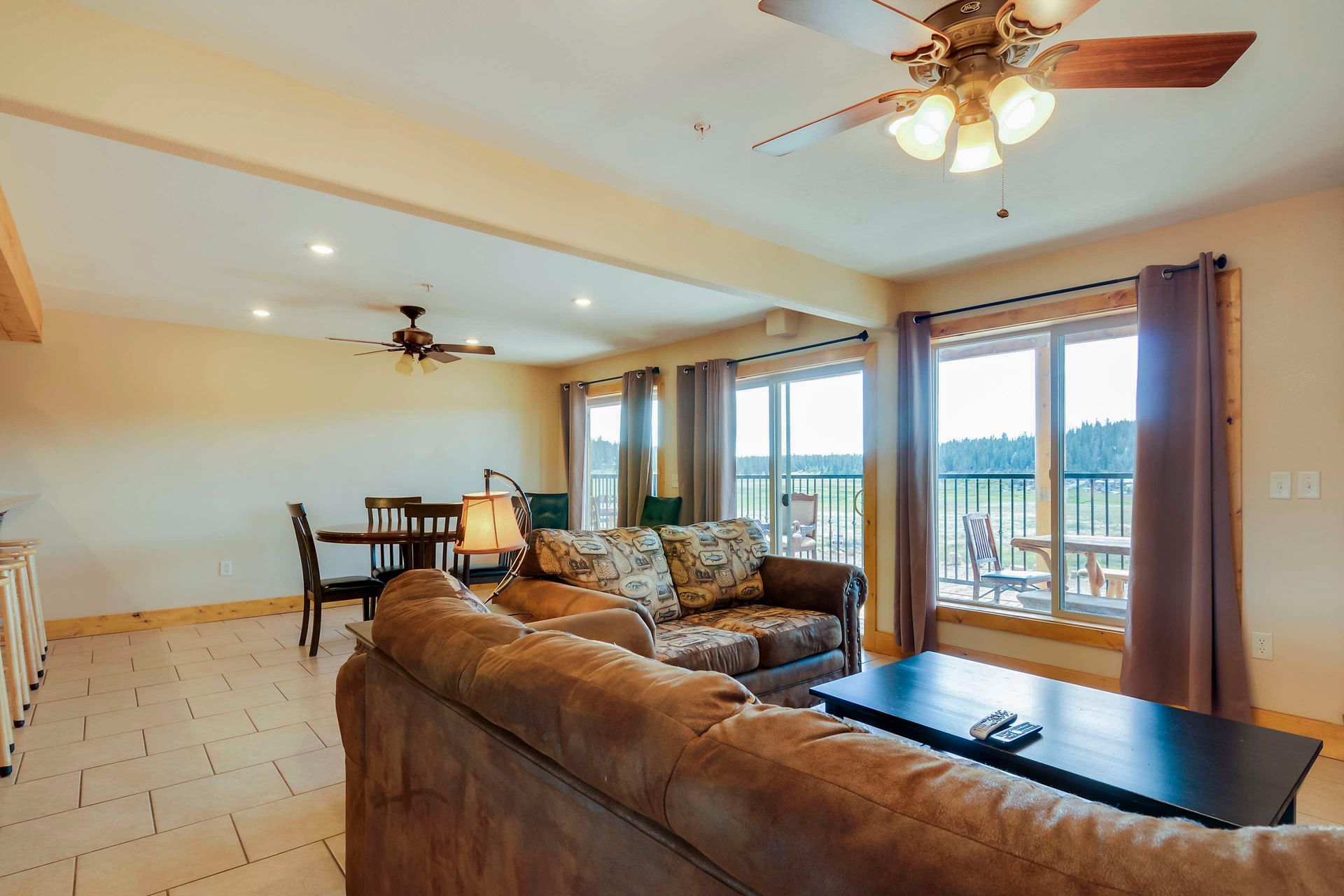 Spacious living room with brown leather sofa, dining table, and large windows overlooking a green landscape.