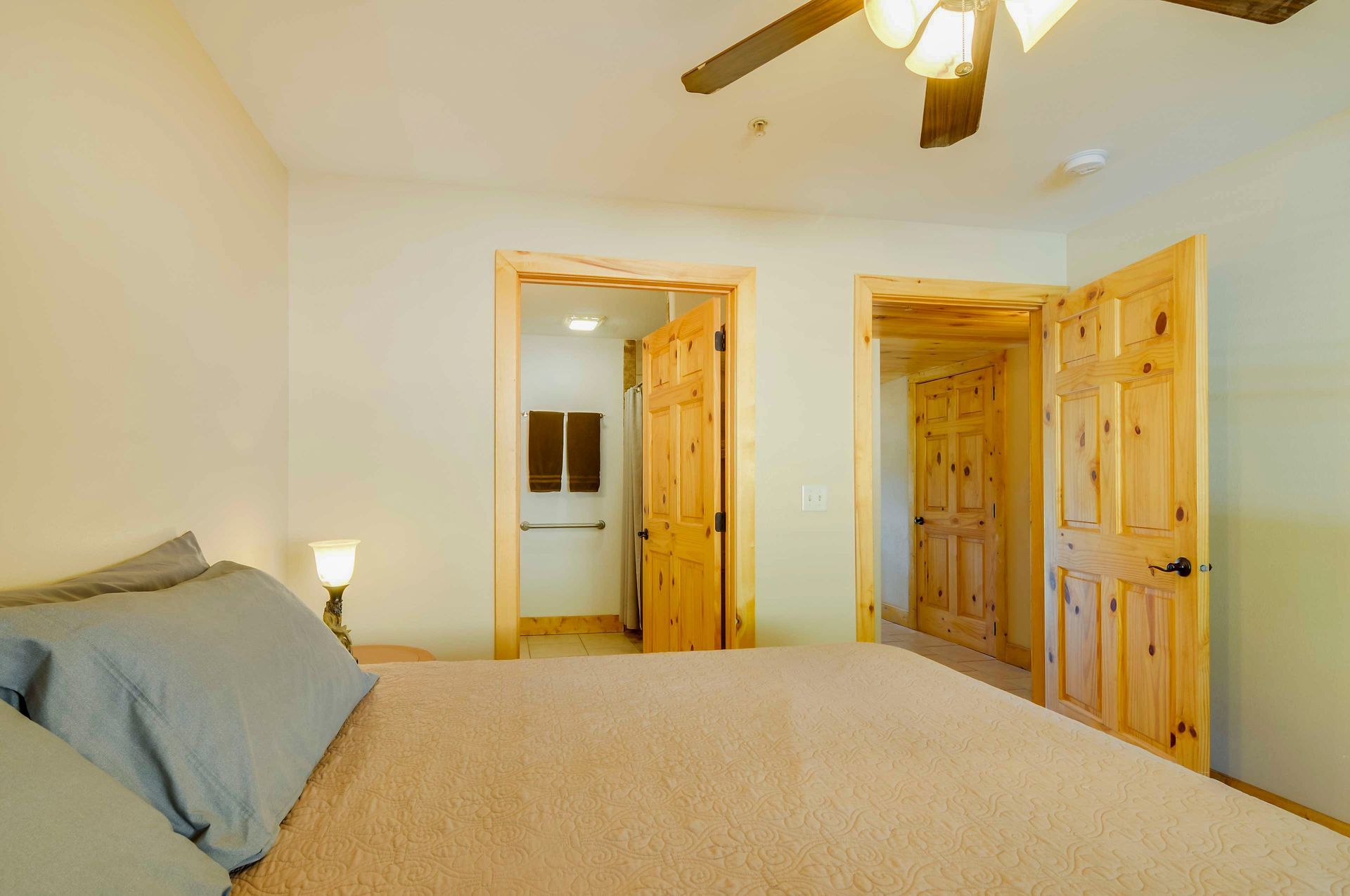 Bedroom with a bed, two wooden doors, and a light-colored ceiling fan. One door leads to a bathroom.
