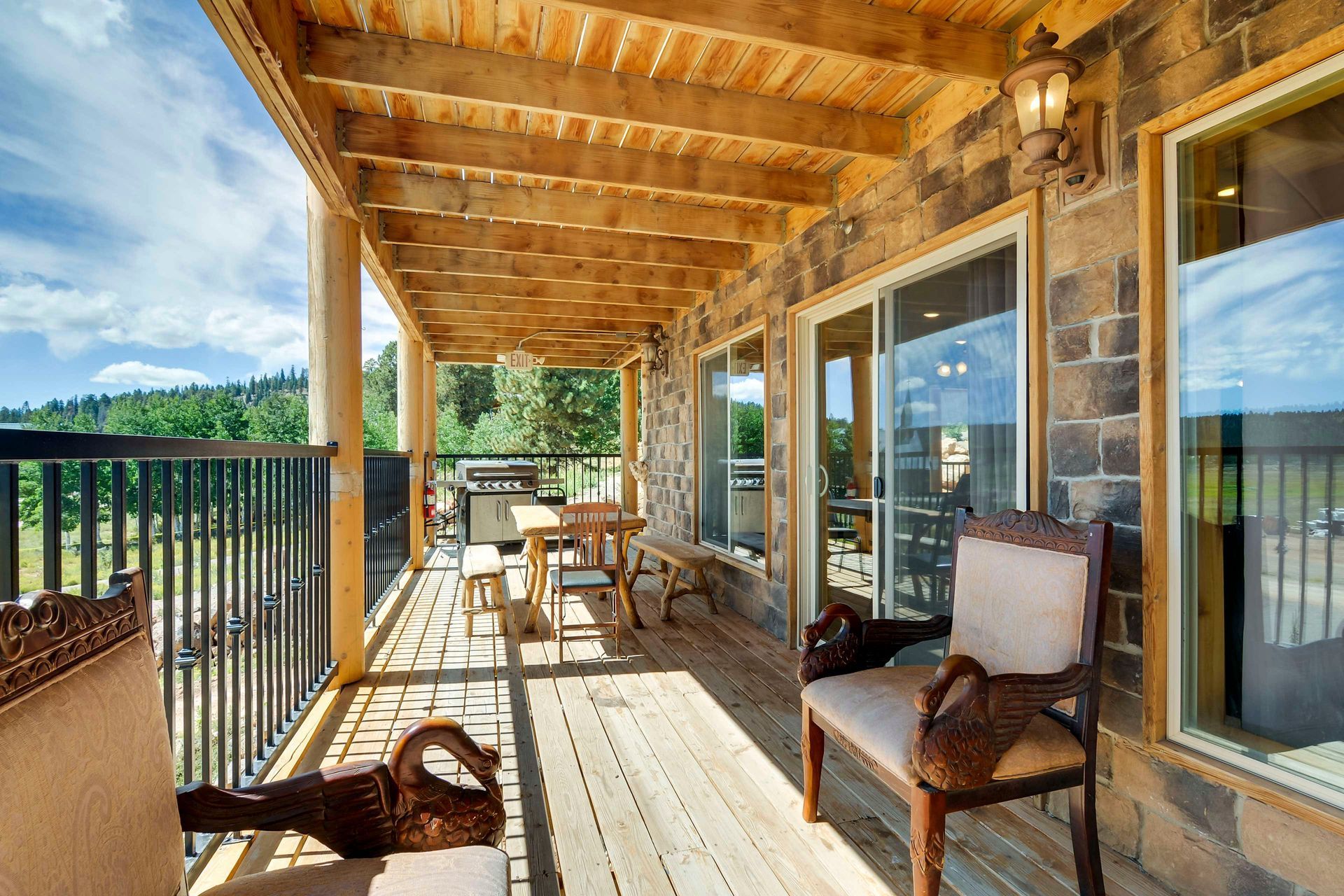 A covered outdoor deck with wood ceiling and floor, stone walls, and a view of a green landscape.