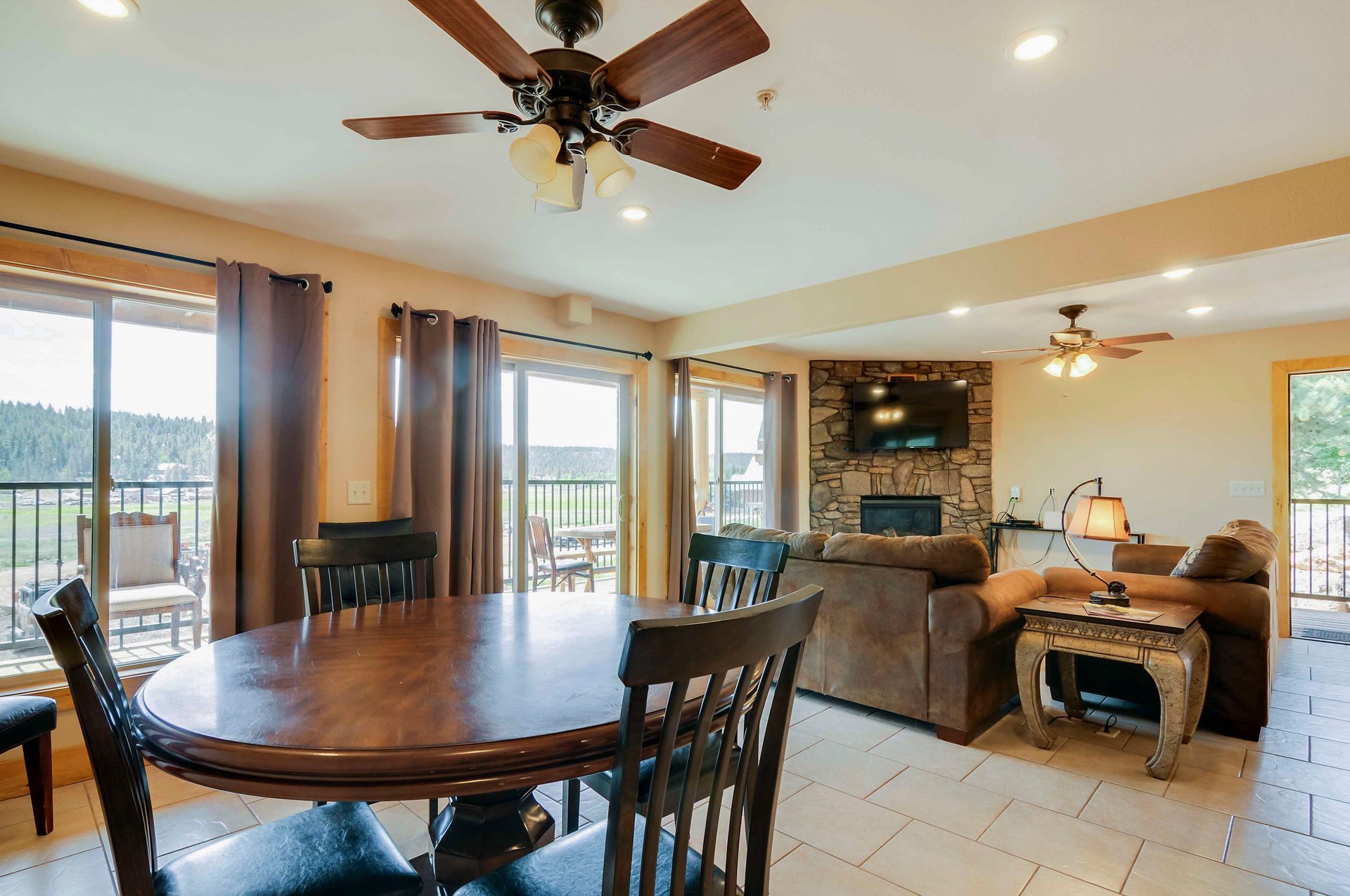A dining area with a round wooden table and chairs, leading to a living room with a fireplace and balcony access.