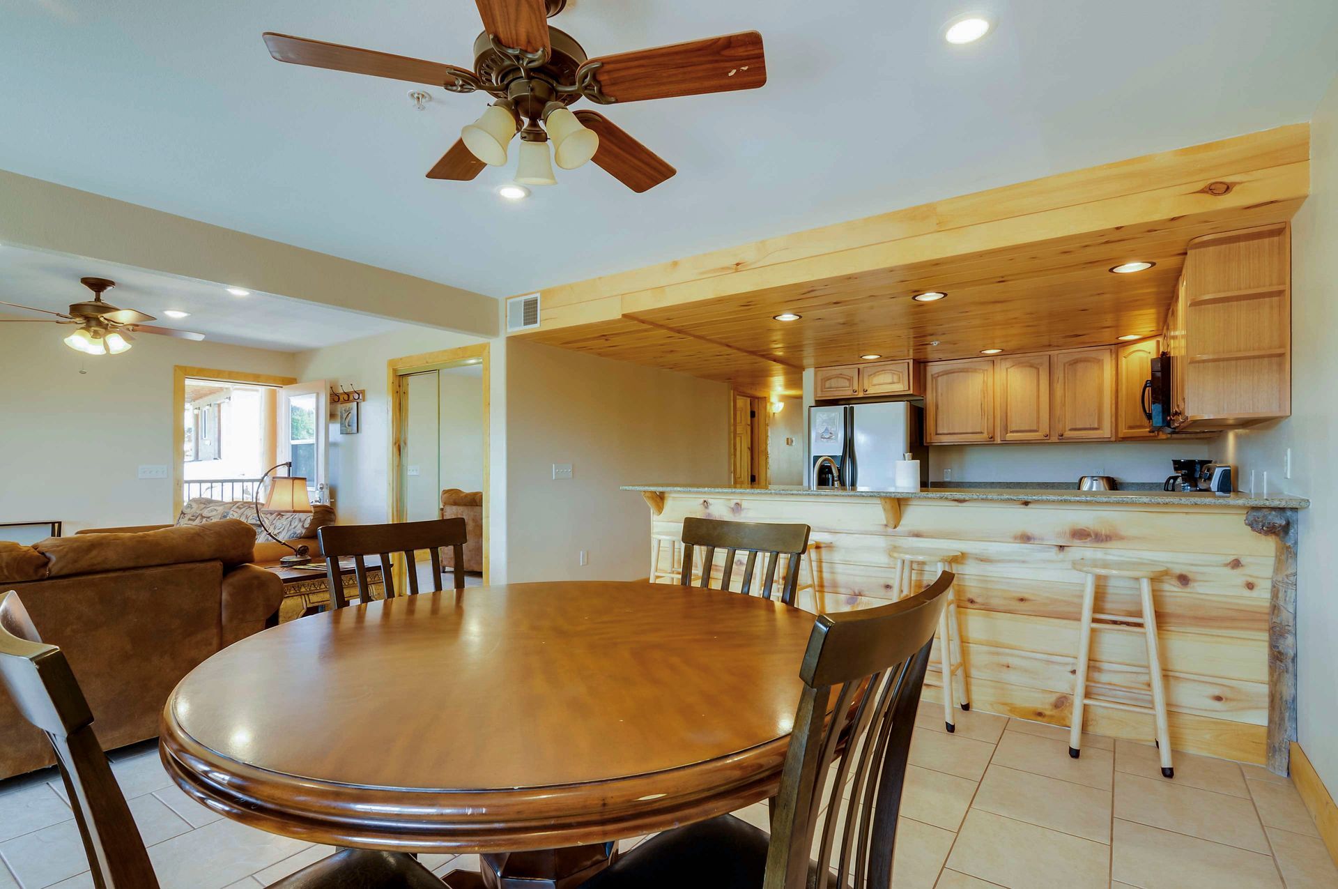 Dining area with round wooden table and chairs, open to a kitchen with a breakfast bar.