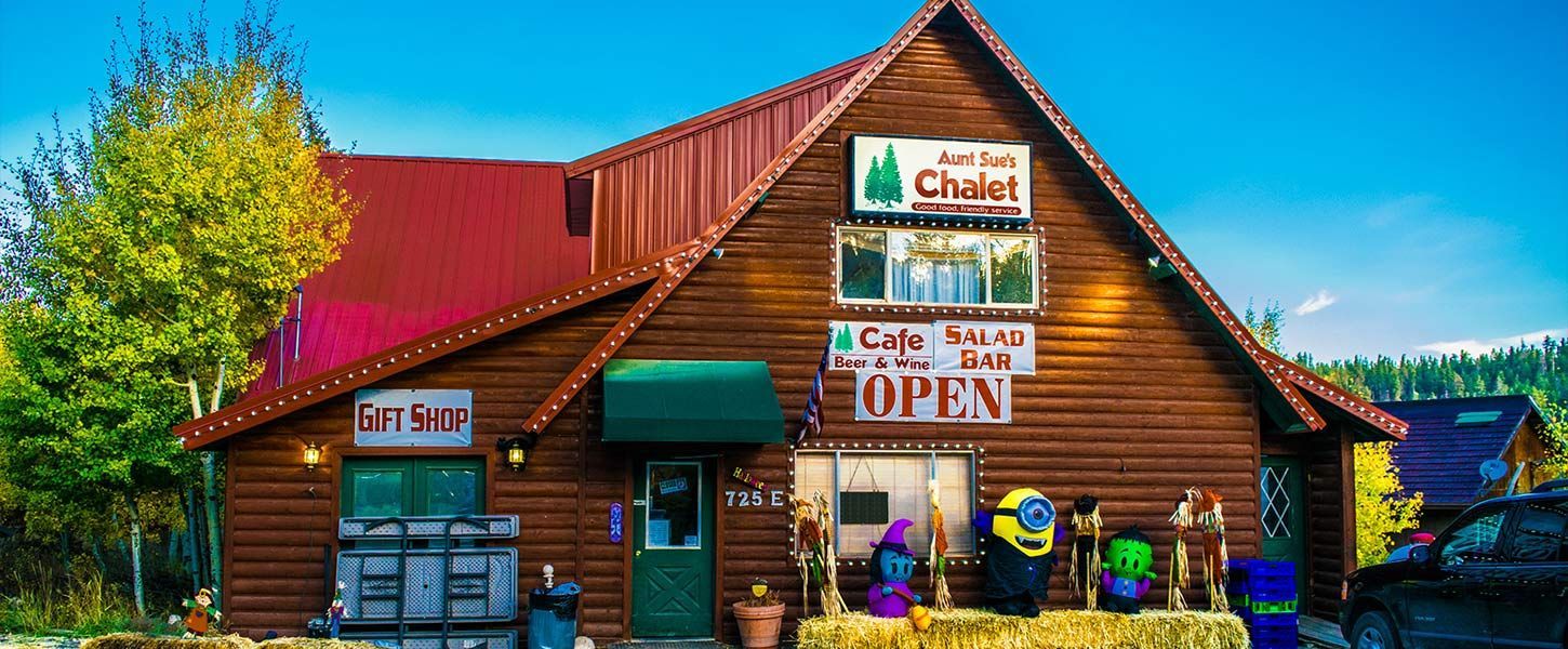 Spacious living room with two patterned sofas, a kitchen, and a dining area. Brown and beige tones with a ceiling fan.