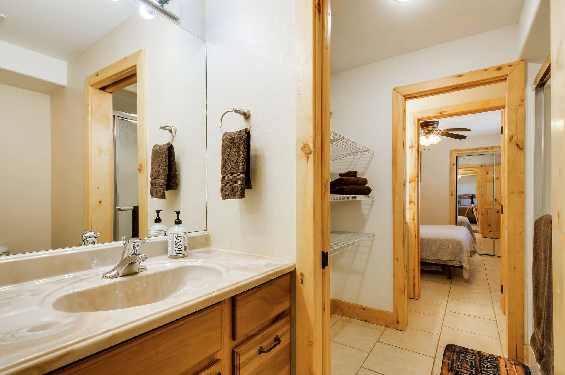 Bathroom with a sink, mirror, and a doorway leading to a bedroom with a bed. Light wood frames the doors and mirror.