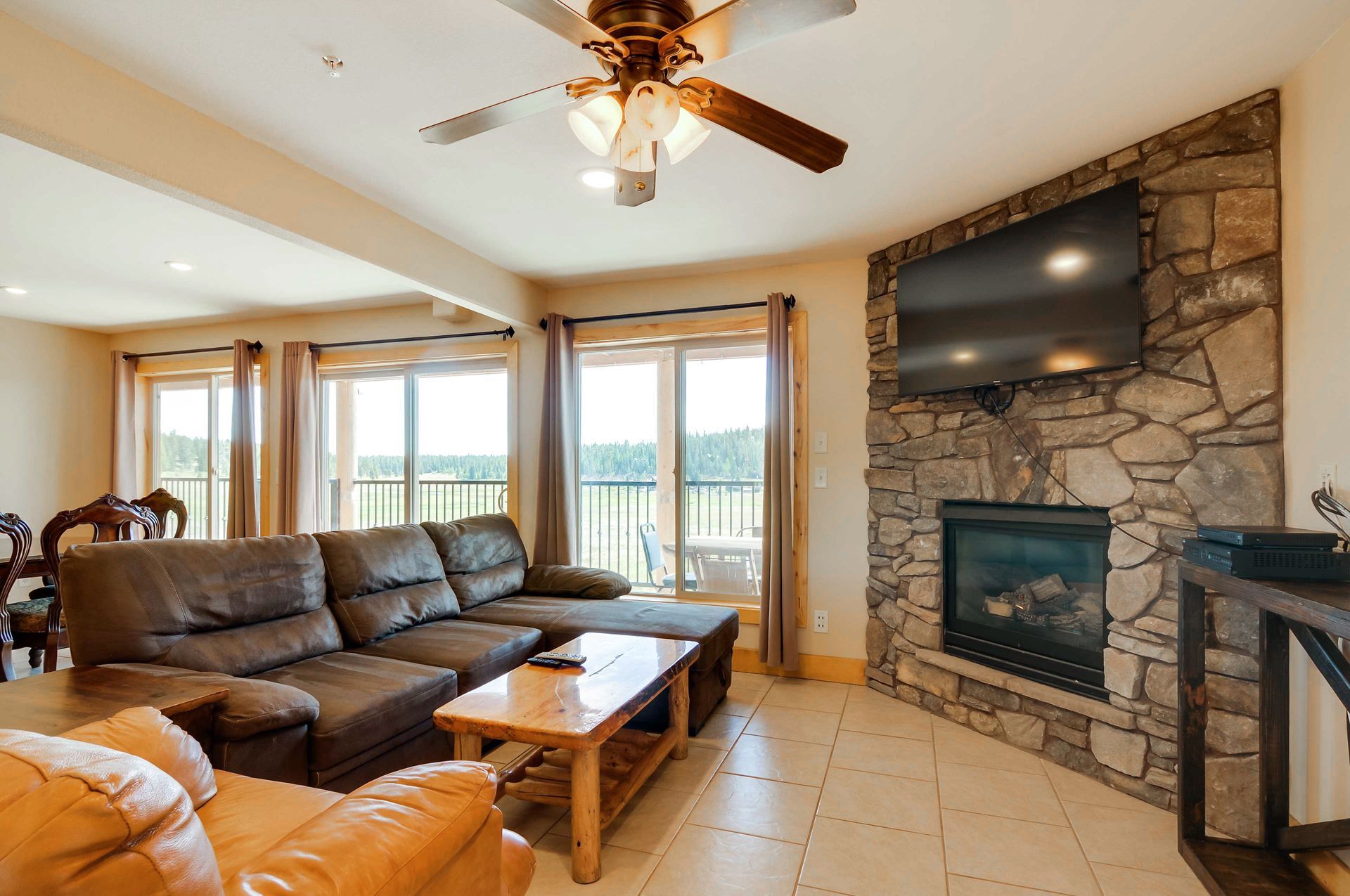 Spacious living room with a leather sectional, fireplace, large TV, and windows overlooking a balcony.
