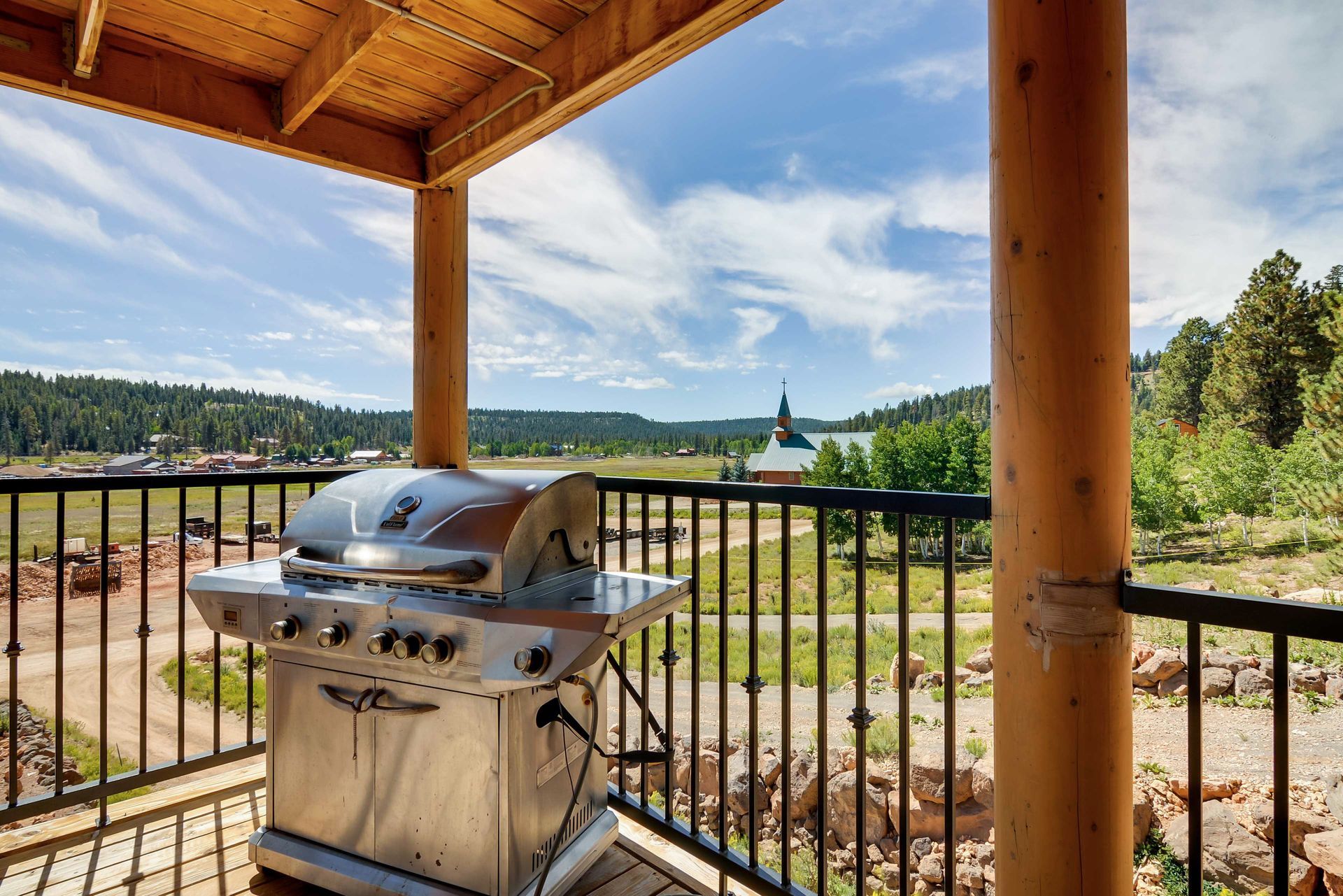 A stainless steel grill on a balcony overlooking a scenic landscape with trees, a lake, and a church in the distance.