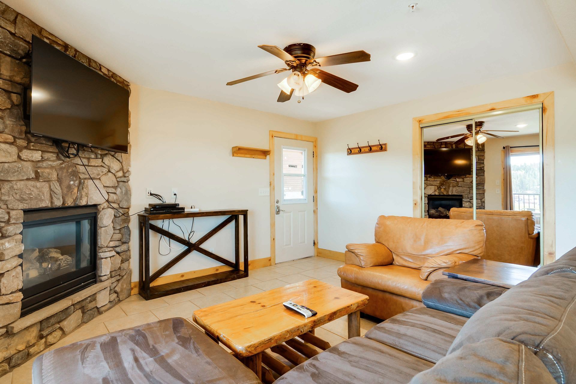 Cozy living room with stone fireplace, brown leather couch, wooden coffee table, and a mirrored wall reflecting the space.