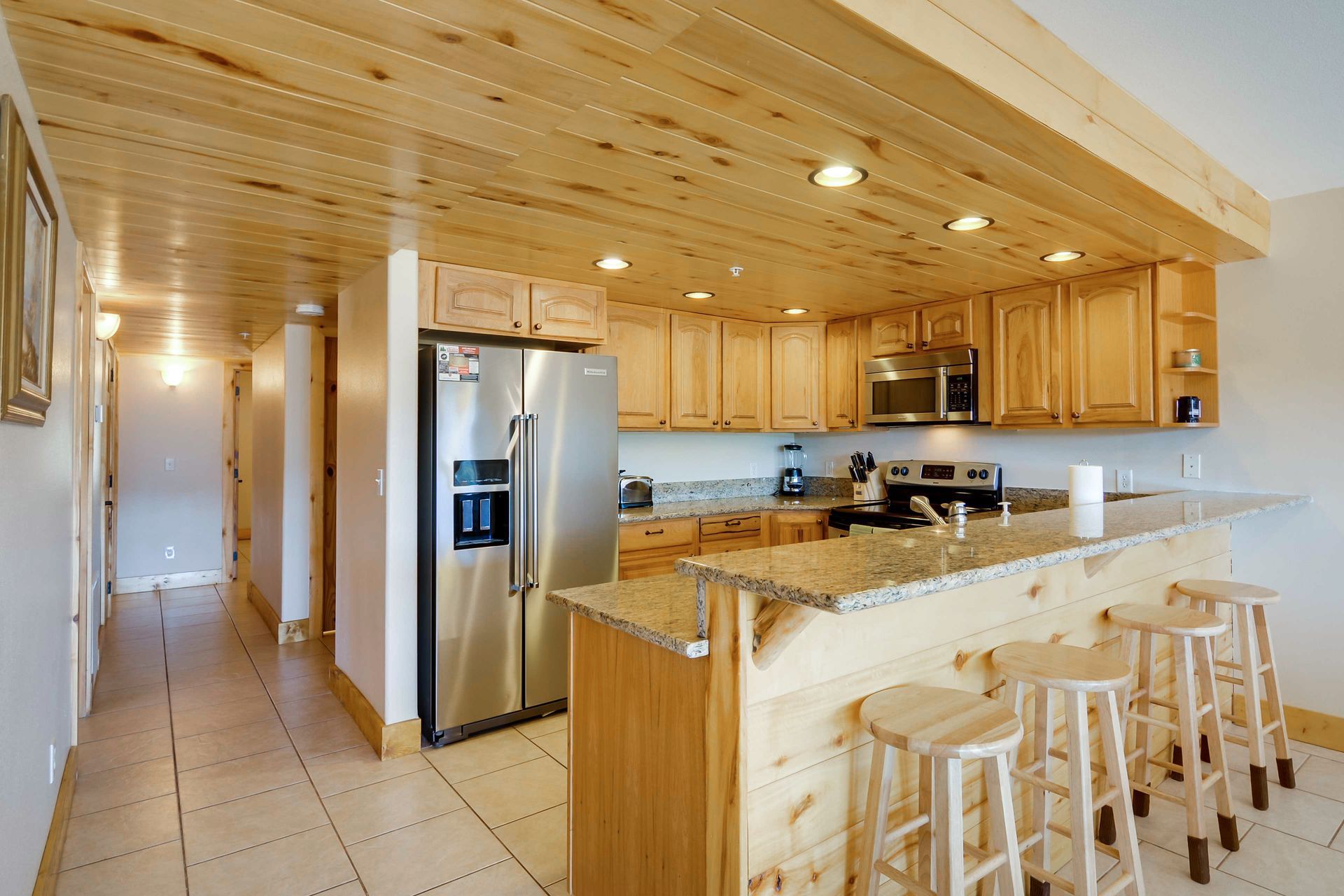 A kitchen with light wood cabinets, a stainless steel refrigerator, and a breakfast bar with stools.