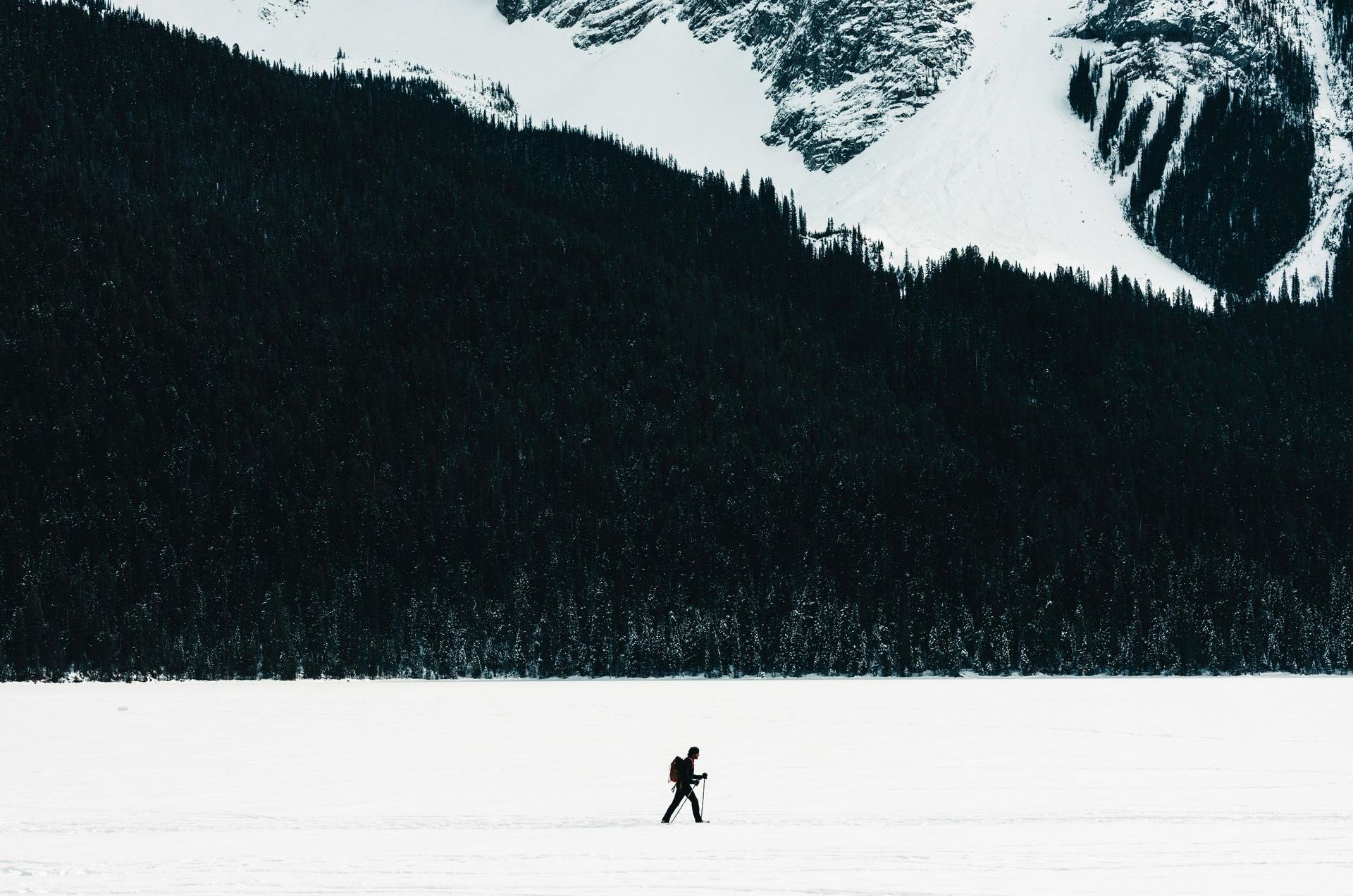 A lone person walks across a frozen lake toward a snow-covered mountain in a winter landscape.