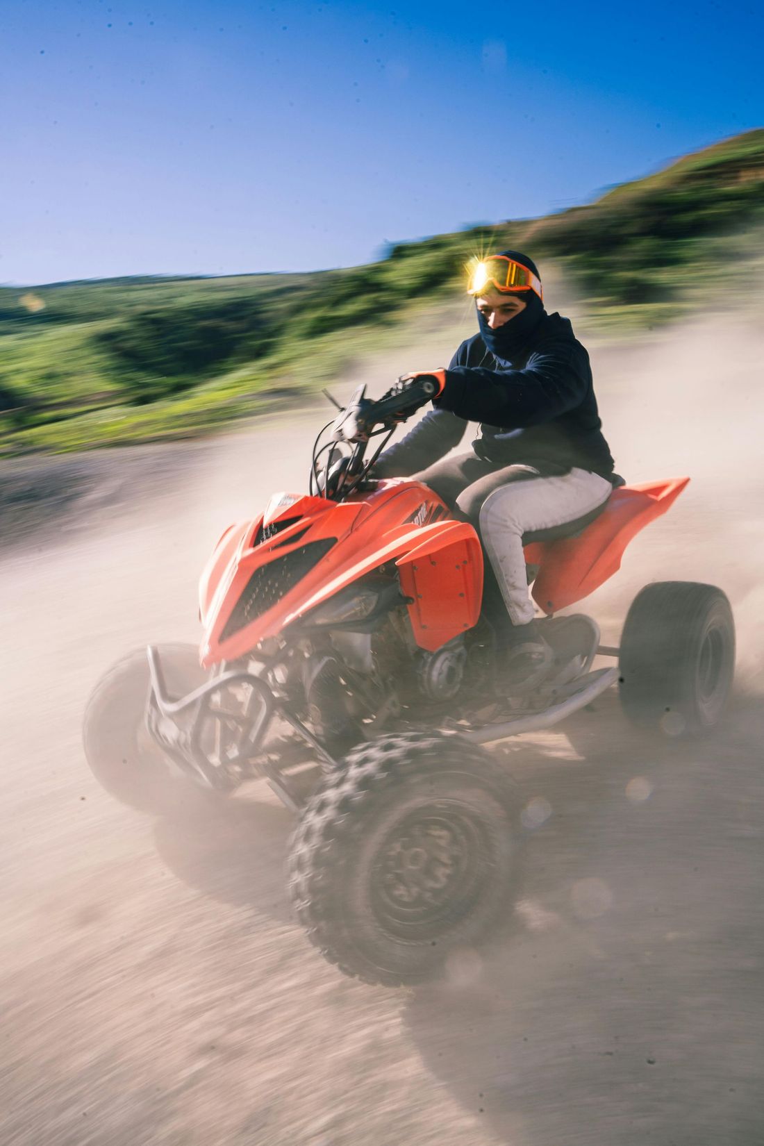 Person riding a red ATV, kicking up dust on a dirt path. They wear a helmet and dark clothing.