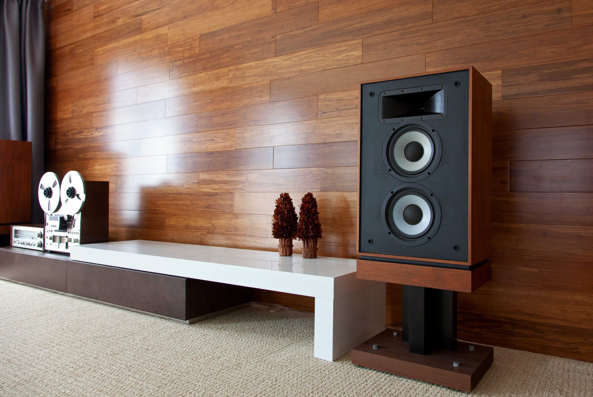 A speaker is sitting in a living room next to a wooden wall.