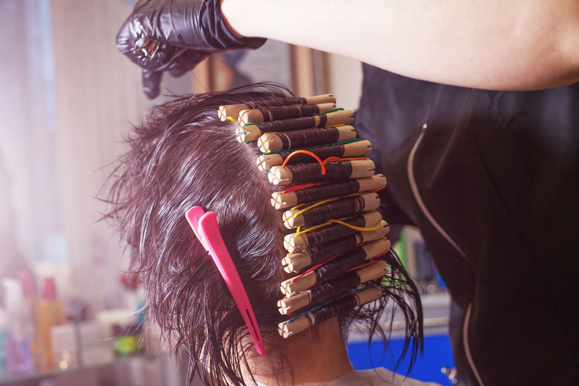 Person's wet hair with perm rods, being worked on by a gloved hand. Pink clip in hair.