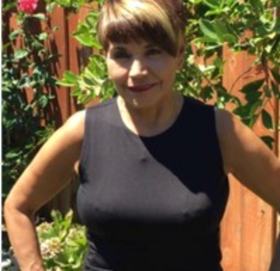 Woman in black sleeveless top outdoors, arms at sides, short hair, sunny.