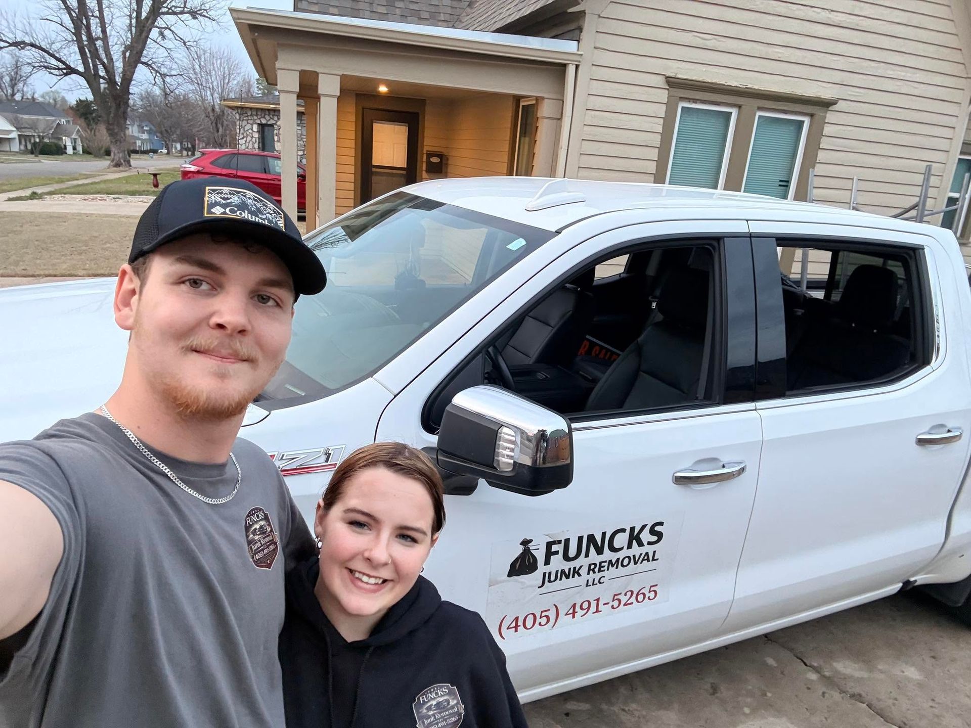 Two smiling people posing beside a white work truck parked in a driveway.