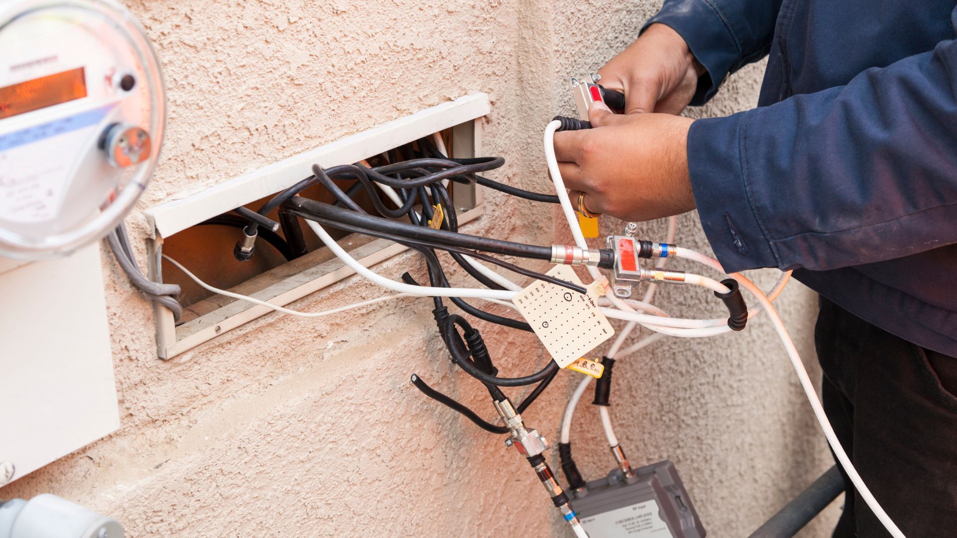 A man is working on a meter with a bunch of wires coming out of it.