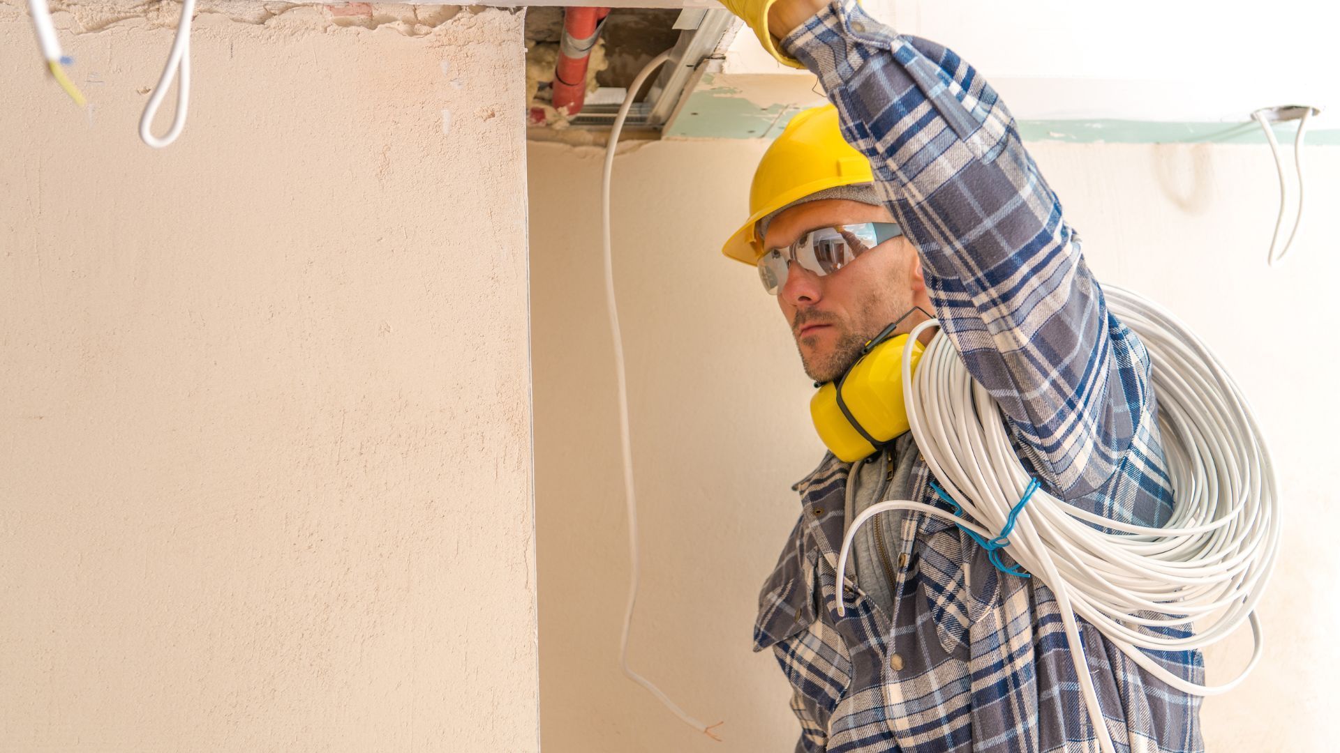 A man wearing a hard hat and headphones is working on a ceiling.