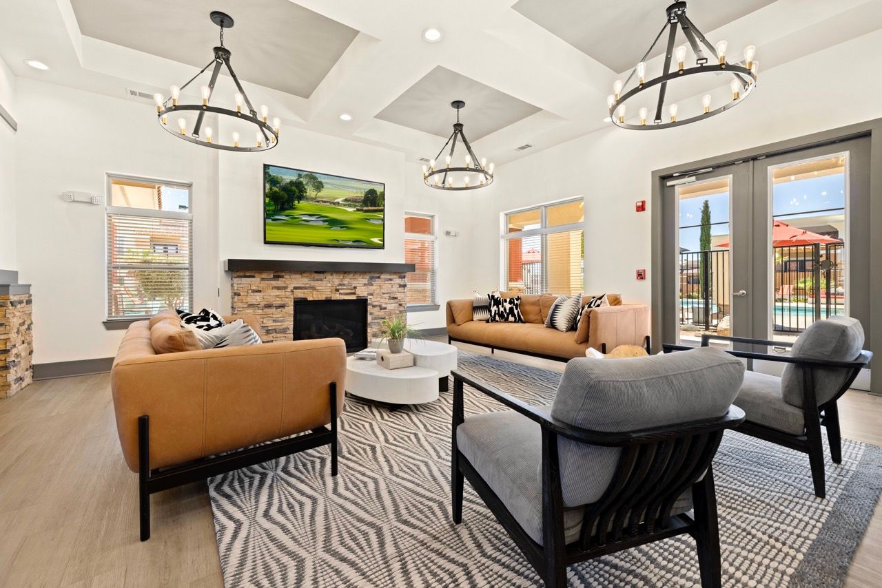 Interior community lounge with tan couches, a stone fireplace, and round chandeliers.