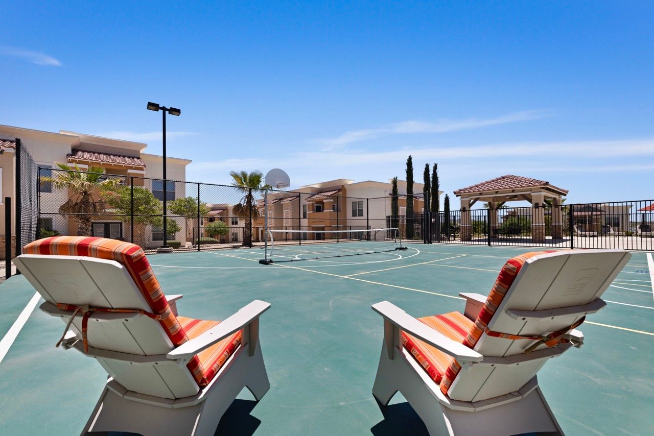 Outdoor recreation court with two striped lounge chairs, a net, and surrounding beige apartment buildings.