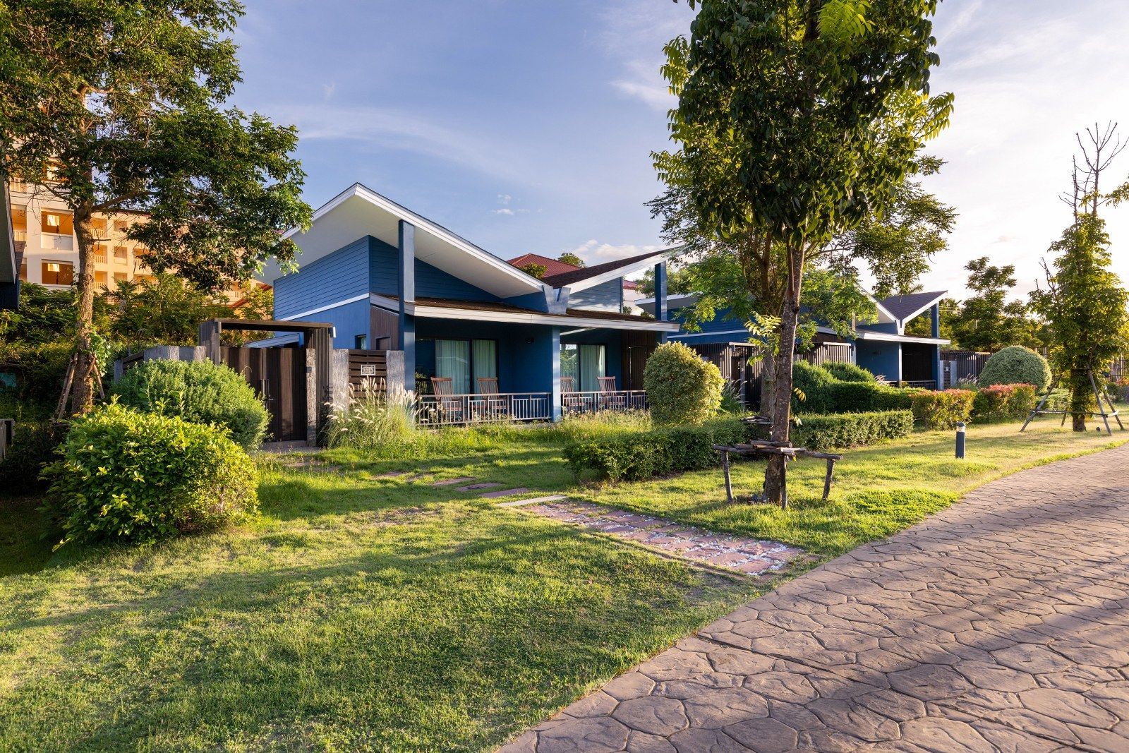Blue bungalows with white roofs, green lawns, and a paved pathway under a sunny sky.