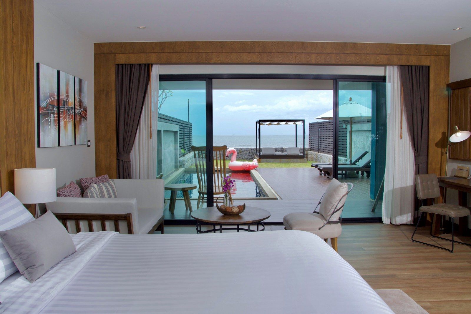 Bedroom with sliding door to a patio with pool, ocean view. Light wood accents, sofa, desk, and flamingo float.
