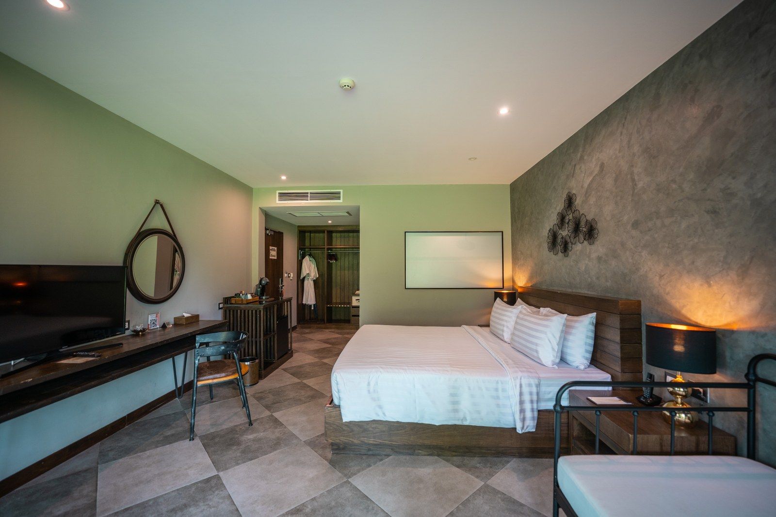 Hotel bedroom with a bed, desk, mirror, and a bathroom visible.