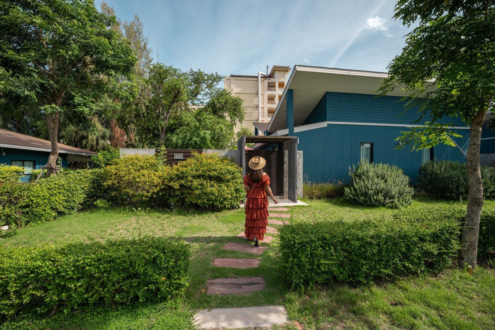 Woman walks towards a blue building with a pathway through a garden.