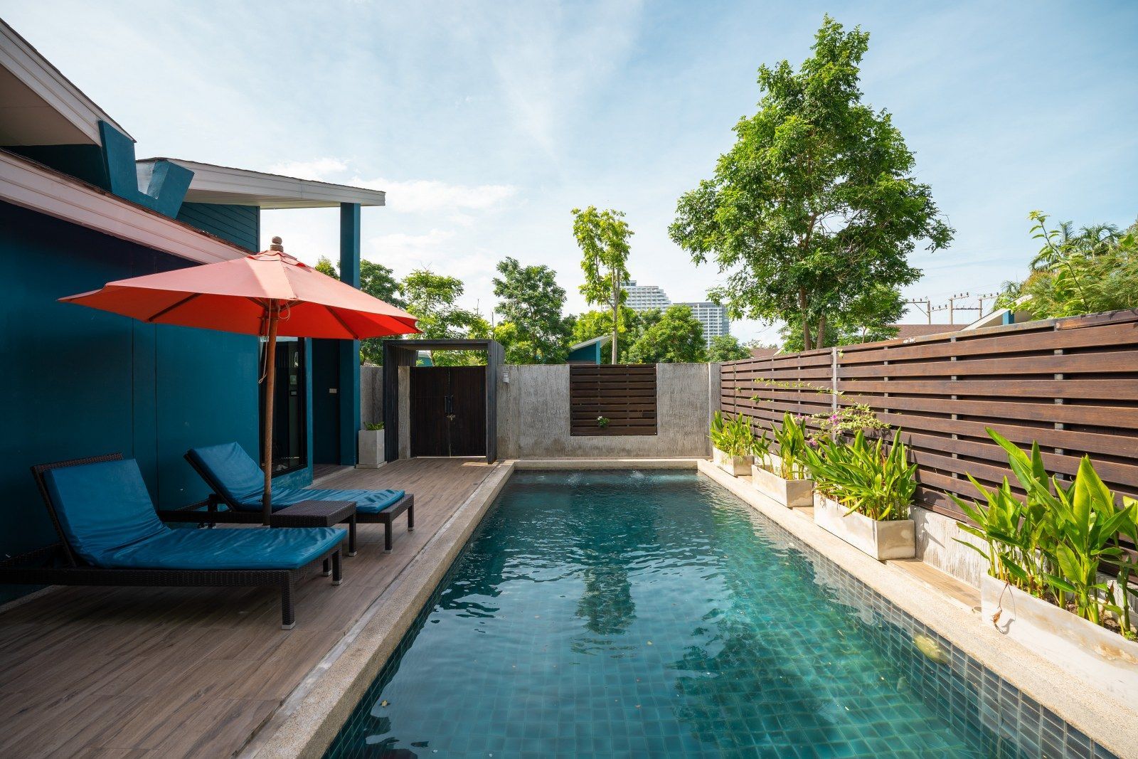 Pool area with lounge chairs, orange umbrella, and wooden fence.