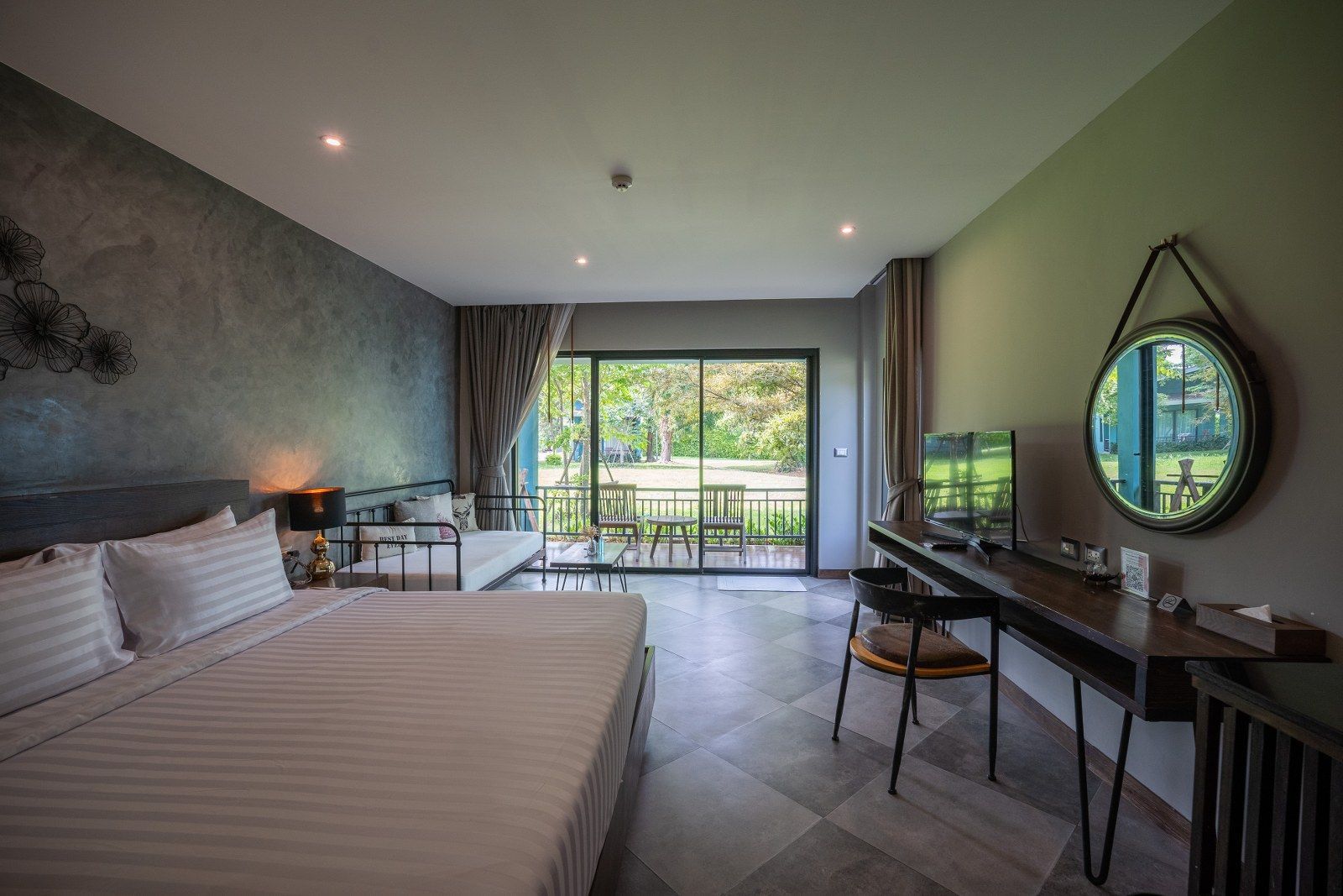 Hotel room with bed, sofa, desk, and sliding glass door overlooking greenery.