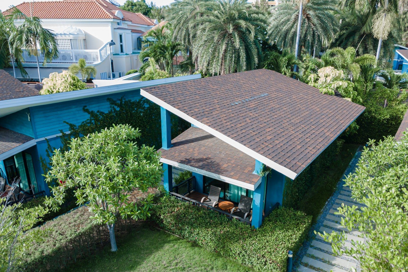 Blue building with brown roof surrounded by green trees and grass.