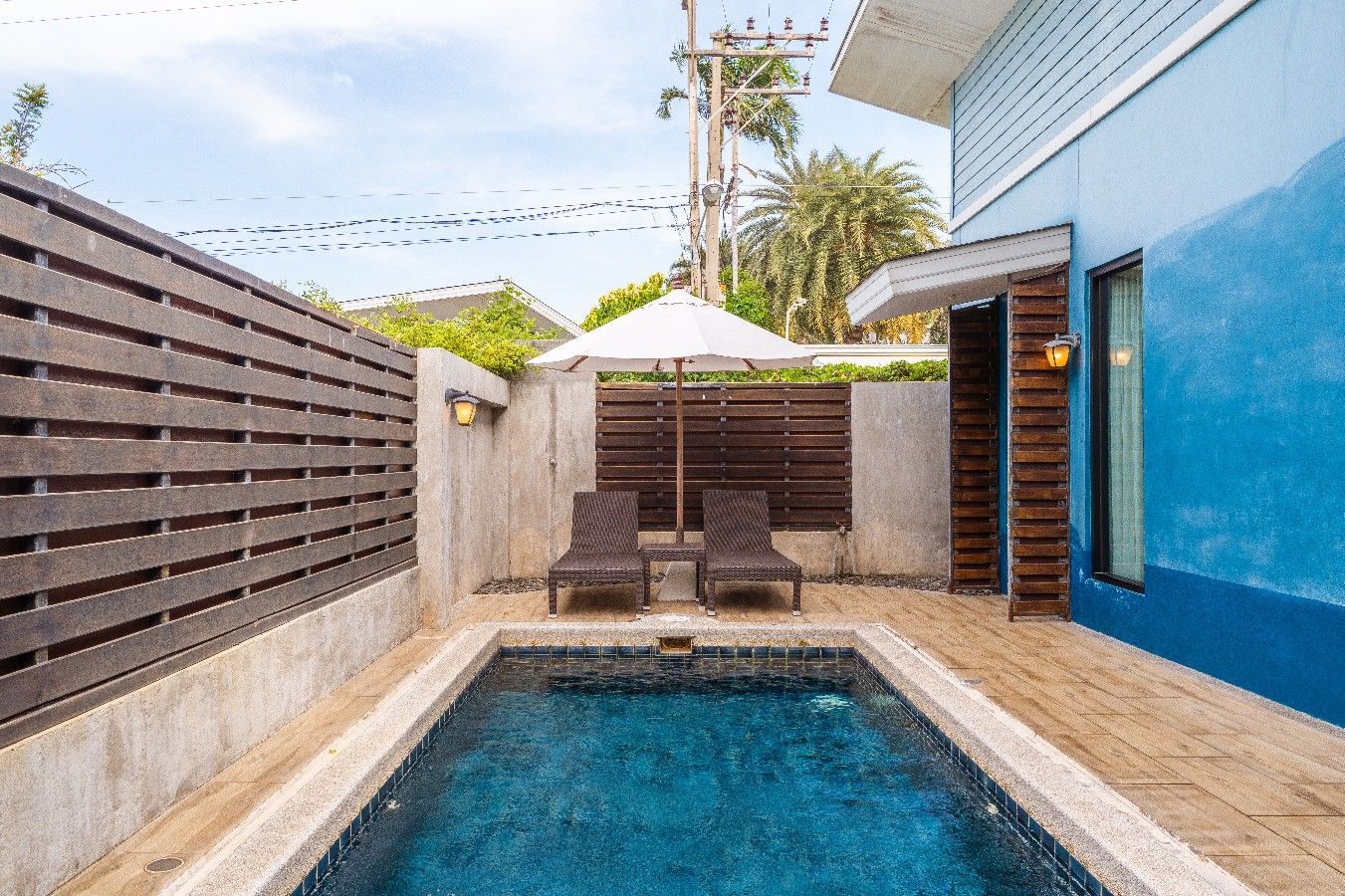Small private pool area with two lounge chairs under an umbrella, blue exterior wall.