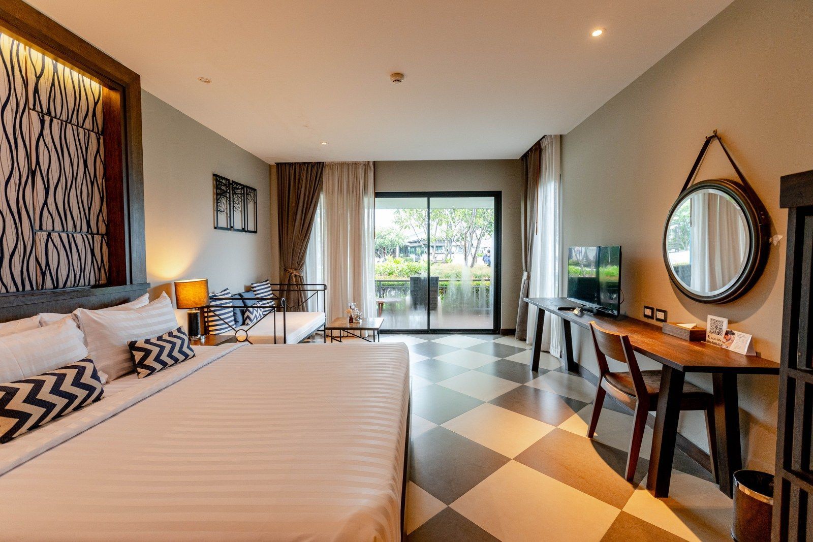 Hotel room with king bed, desk, and balcony access. Beige, brown, and gray color scheme.